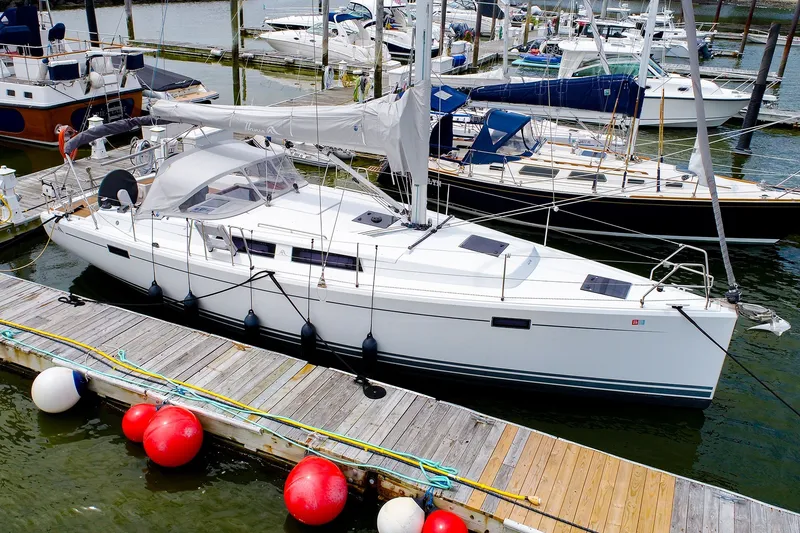 The Image of 2016 Hanse 385 sailboat docked at marina, surrounded by other boats and colorful buoys. - 0