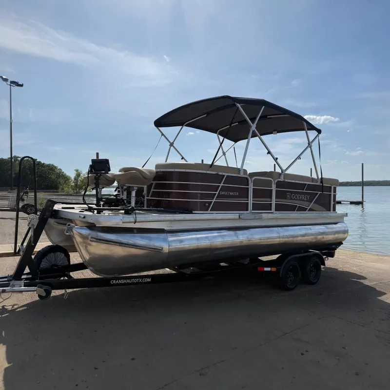 Slide: The Image of 2021 Godfrey Sweetwater 2286 FS pontoon boat on trailer by a lake. - 0
