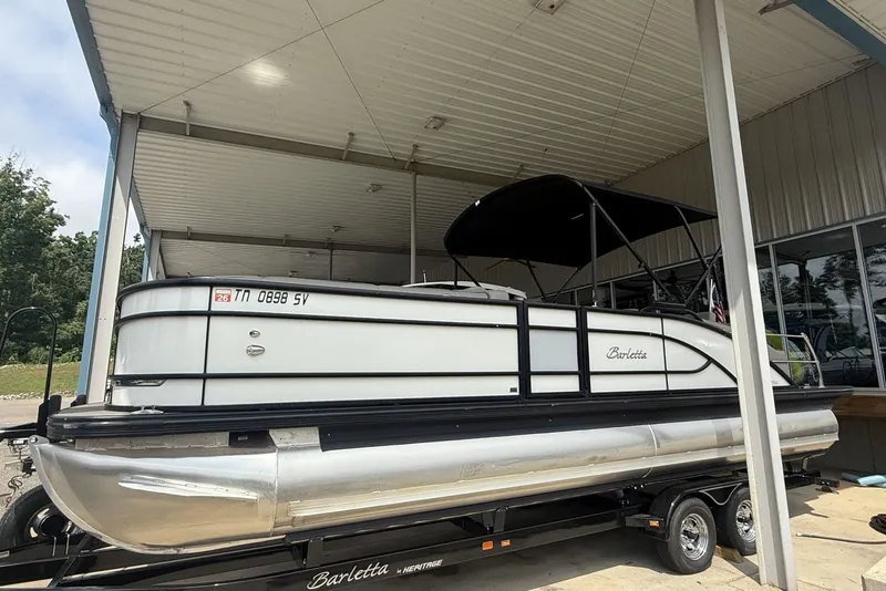 The Image of 2021 Barletta L25U pontoon boat on trailer under a metal canopy. - 1
