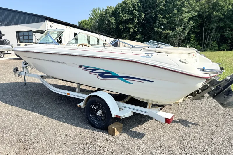 Slide: The Image of 1995 Searay 195 boat on trailer, parked outdoors near a building and trees. - 2