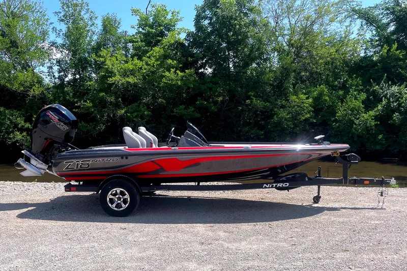 The Image of A 2024 Nitro Z18 boat on a trailer, set against a wooded backdrop. - 1