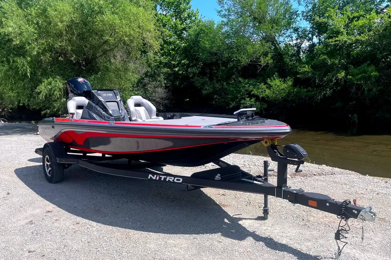 Slide: The Image of A 2024 Nitro Z18 boat on a trailer, surrounded by trees and a river in the background. - 2
