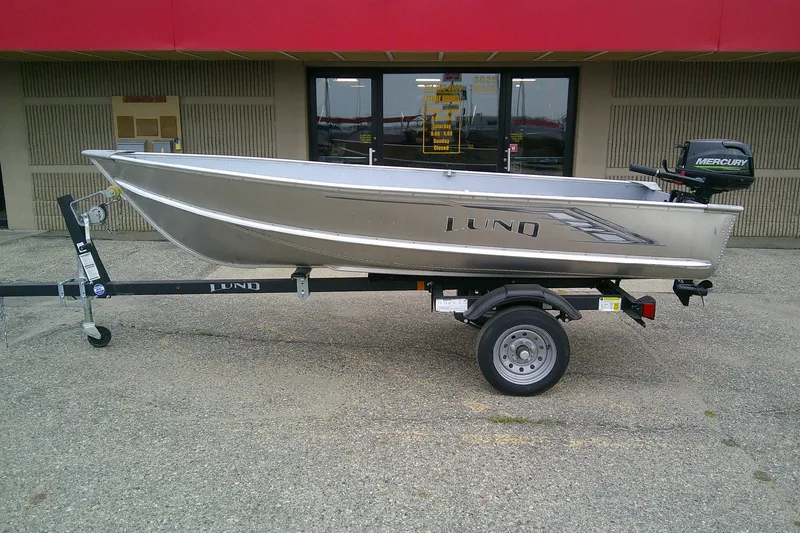 The Image of 2022 Lund A-12 aluminum boat on trailer, parked outside a building. - 0
