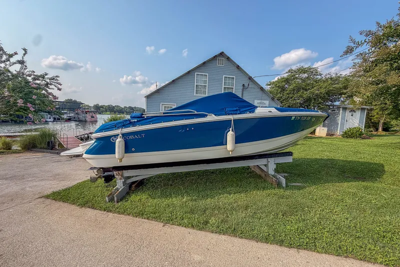 Slide: The Image of 2011 Cobalt 210 boat on trailer, blue cover, near lake and house. - 1