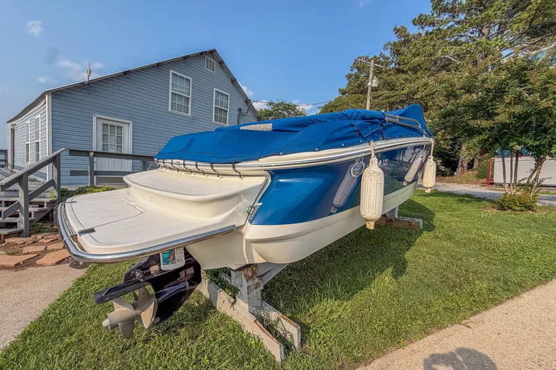 Slide: The Image of 2011 Cobalt 210 boat with blue cover, parked on grass near a house. - 2