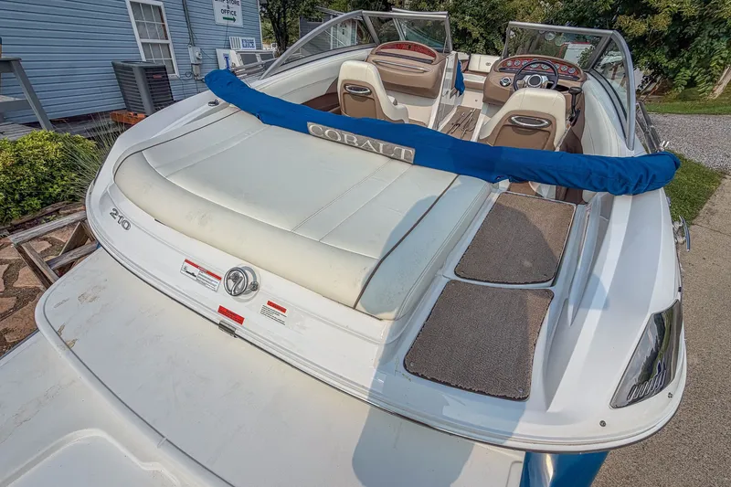 Slide: The Image of 2011 Cobalt 210 boat with white seating and blue cover, parked near a house. - 20
