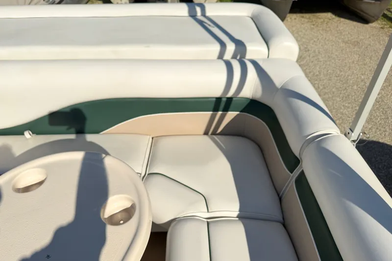 Slide: The Image of 2006 Godfrey Aqua Patio boat interior with beige and green seating, featuring a round table. - 8