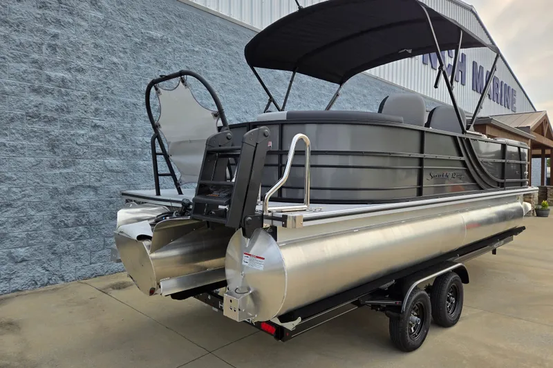 Slide: The Image of A modern pontoon boat with a black canopy and silver hull sits on a trailer. - 2