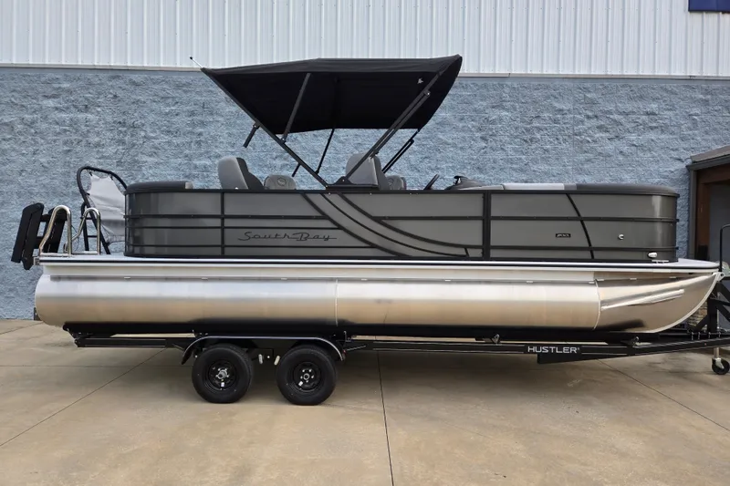 The Image of A modern pontoon boat with a black canopy and gray siding sits on a trailer. - 0