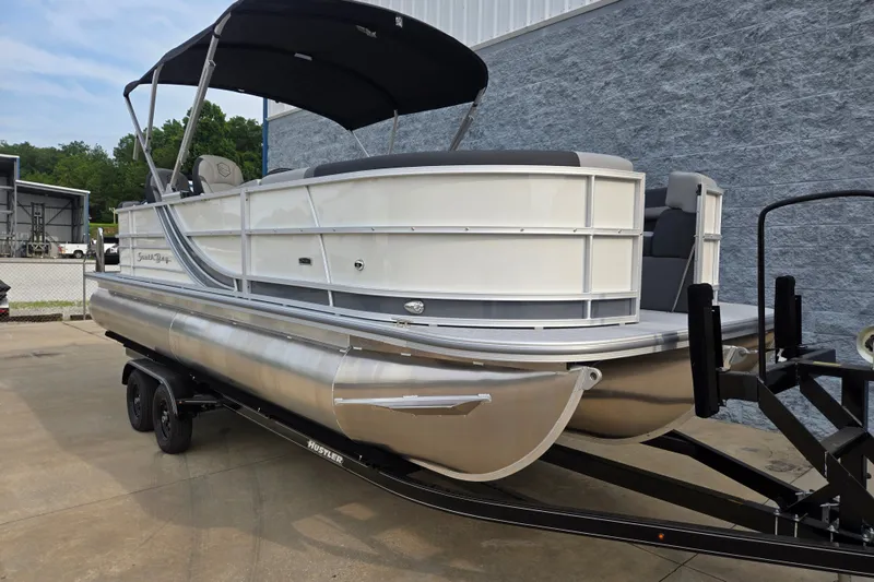 Slide: The Image of A sleek pontoon boat with a black canopy, parked on a trailer in front of a gray building. - 3
