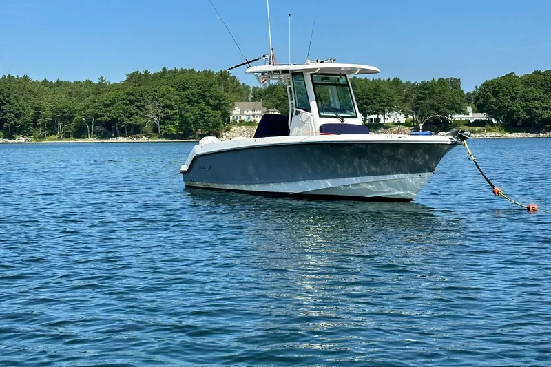 Slide: The Image of 2024 Boston Whaler 250 Outrage boat anchored on calm water with scenic forest backdrop. - 4