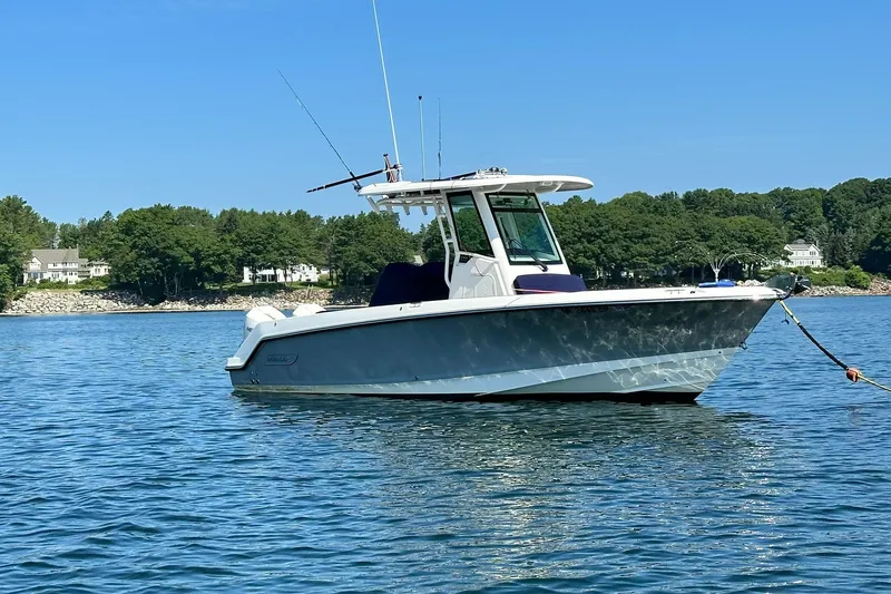 Slide: The Image of 2024 Boston Whaler 250 Outrage boat anchored on calm water, surrounded by lush greenery. - 2