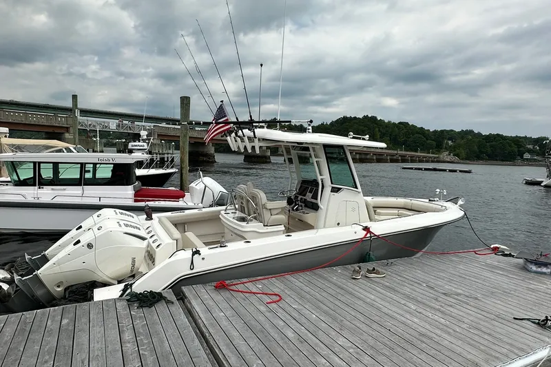 Slide: The Image of 2024 Boston Whaler 250 Outrage docked, featuring fishing rods and twin engines. - 5