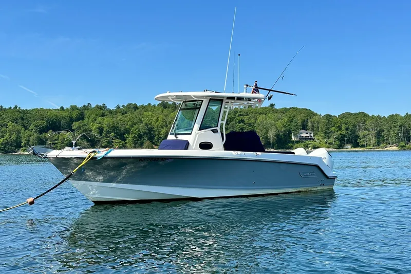 Slide: The Image of 2024 Boston Whaler 250 Outrage boat on calm water with forested shoreline. - 3