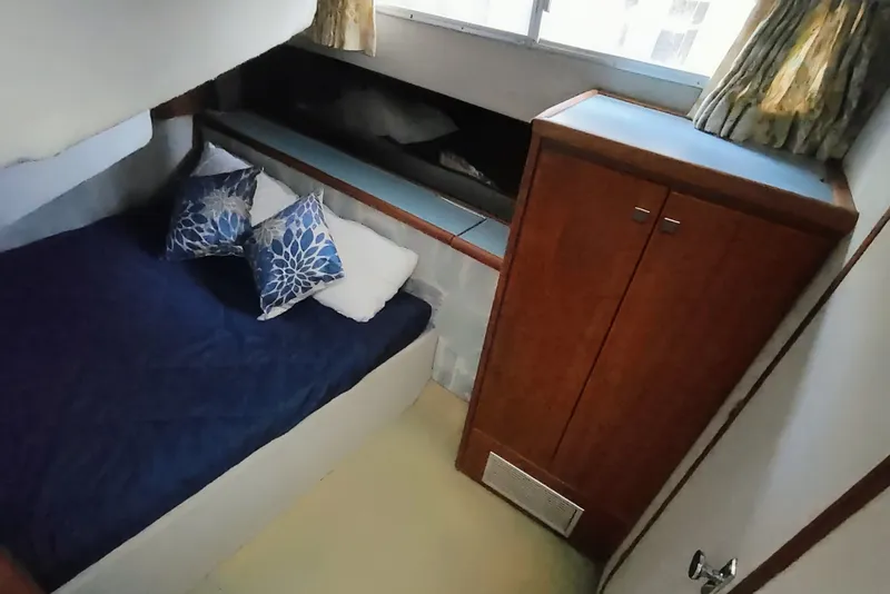 Slide: The Image of The 1988 Bayliner 3818 Motoryacht cabin features a cozy bed with blue pillows and a wooden cabinet. - 34