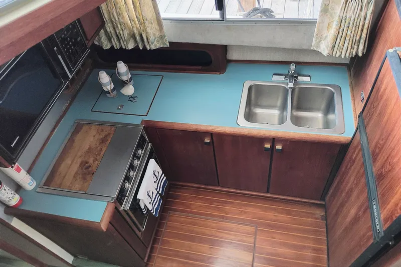 Slide: The Image of The 1988 Bayliner 3818 Motoryacht's kitchen features a sink, stove, and wooden cabinets. - 27