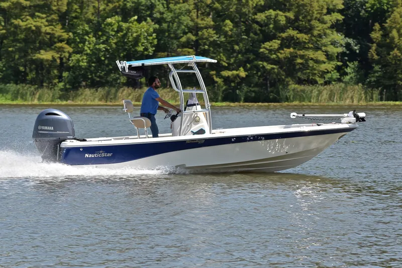 Slide: The Image of 2019 NauticStar 215 XTS Shallow Bay boat cruising on a lake with lush green trees. - 3