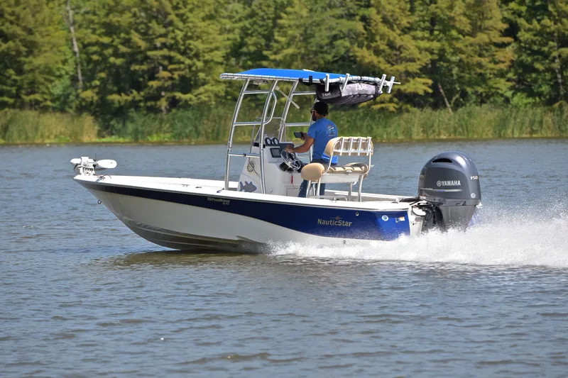 Slide: The Image of 2019 NauticStar 215 XTS Shallow Bay boat cruising on a lake with lush greenery. - 4