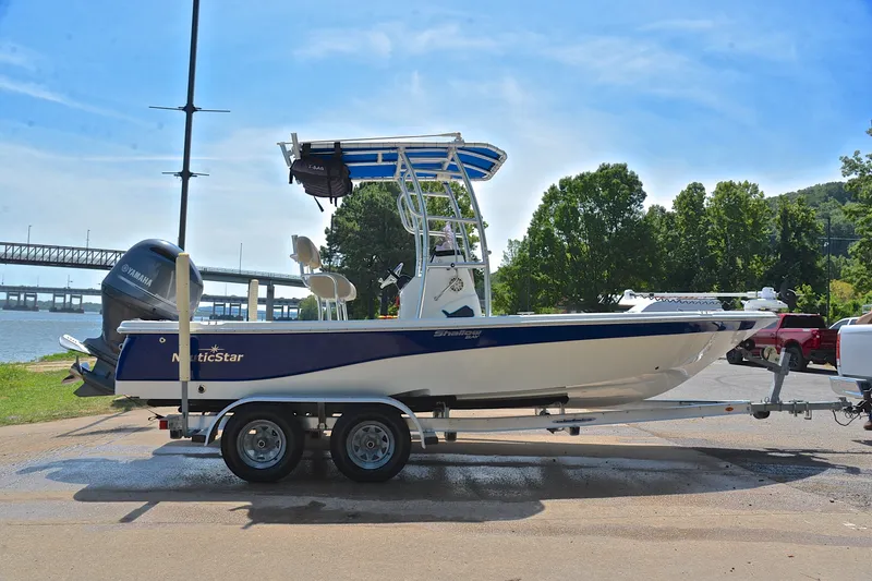 Slide: The Image of 2019 NauticStar 215 XTS Shallow Bay boat on trailer by riverside, sunny day. - 15
