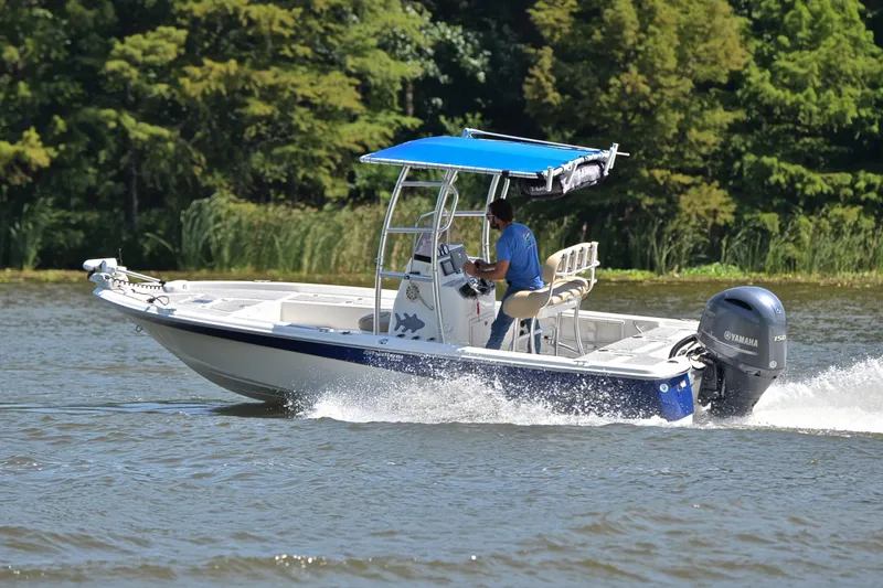 Slide: The Image of 2019 NauticStar 215 XTS Shallow Bay boat cruising on a lake with lush greenery. - 6