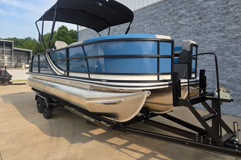 Slide: The Image of A modern pontoon boat with a blue hull and black railing sits on a trailer. - 3
