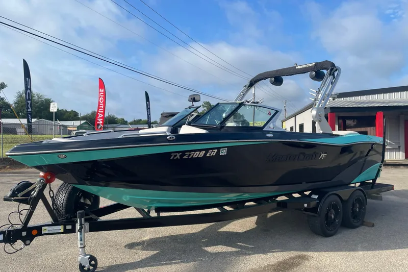 Slide: The Image of 2018 MasterCraft XT23 boat on trailer, black and teal design, parked outdoors. - 4
