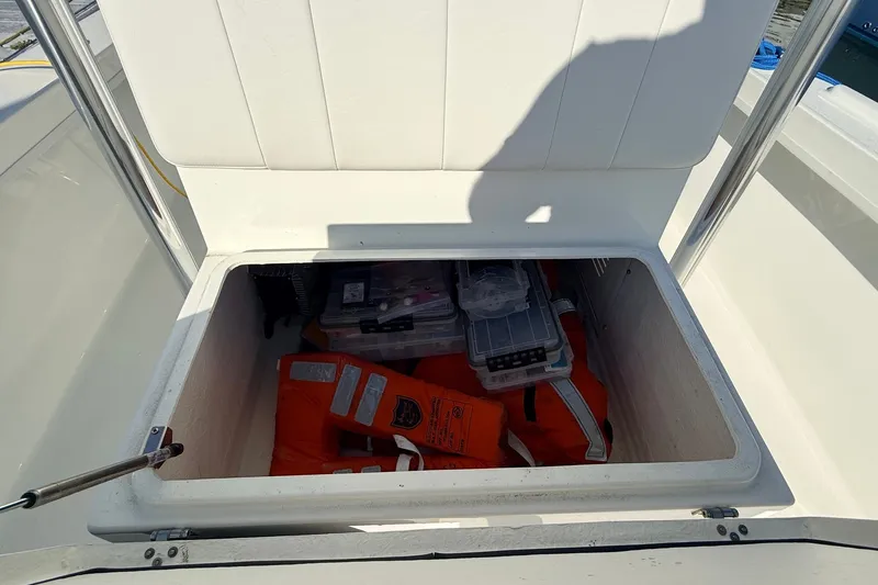 Slide: The Image of Open storage compartment on 2023 Pair Customs 24 Center Console DV, containing life jackets and gear. - 21
