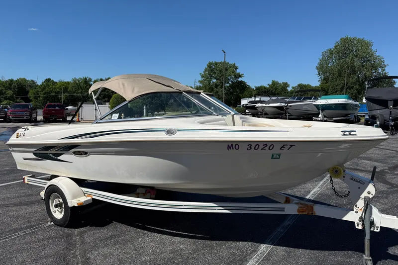 The Image of 2000 Sea Ray 180 Bow Rider boat on trailer in parking lot under clear blue sky. - 1