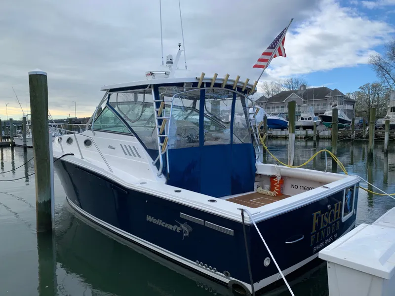 The Image of A 2004 Wellcraft 330 Coastal docked. It features a blue canopy and an American flag. - 0