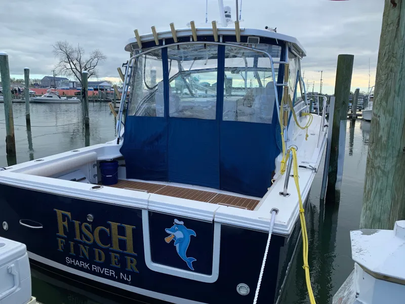 Slide: The Image of A 2004 Wellcraft 330 Coastal docked. It features a blue rear enclosure and fishing rod holders. - 2