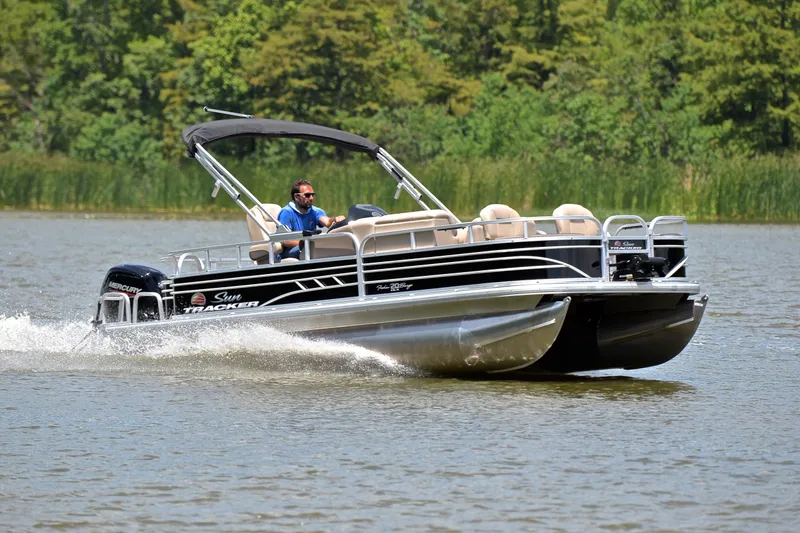 The Image of 2022 Sun Tracker Fishin' Barge 20 DLX cruising on a lake with lush greenery. - 1