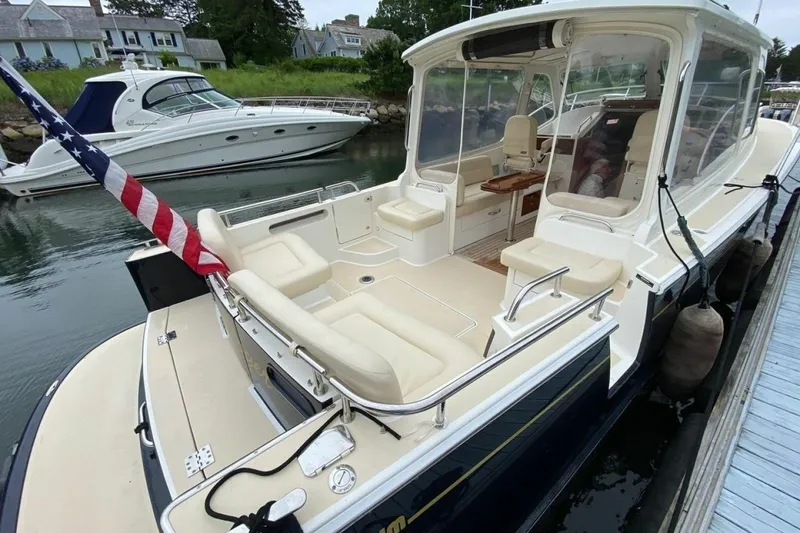 Slide: The Image of 2013 MJM 36z Downeast boat docked, featuring spacious seating and American flag. - 10