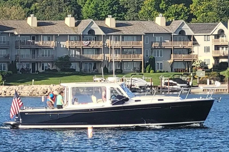 The Image of 2013 MJM 36z Downeast boat cruising near waterfront homes, displaying an American flag. - 0