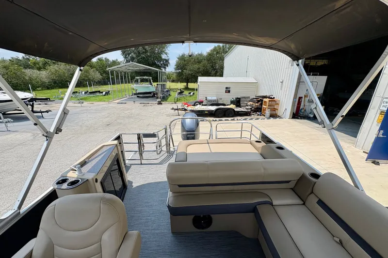 Slide: The Image of 2023 Sweetwater 2286 FSL pontoon boat interior with seating and canopy, parked near a warehouse. - 19