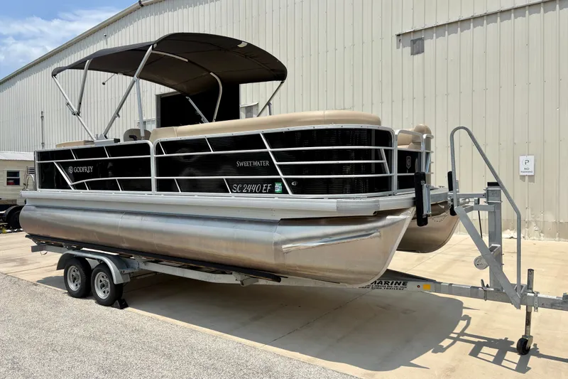 Slide: The Image of 2023 Sweetwater 2286 FSL pontoon boat on trailer, parked outside a warehouse. - 3