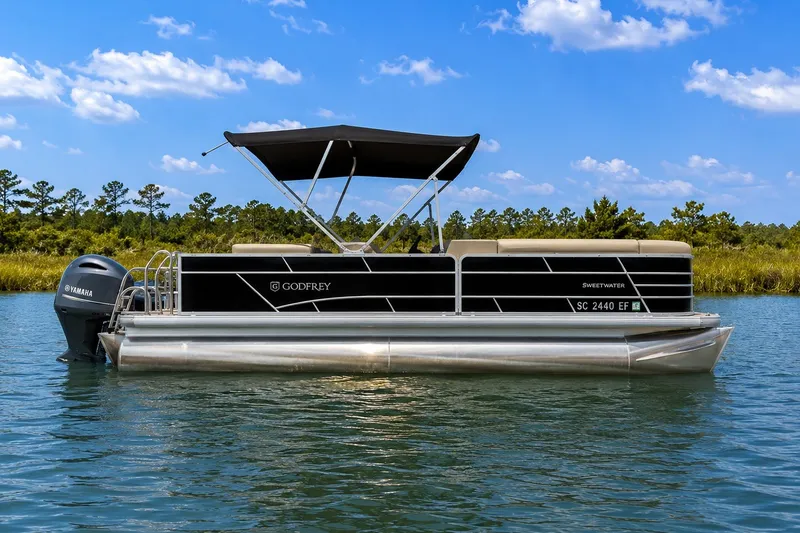The Image of 2023 Sweetwater 2286 FSL pontoon boat on a serene lake with clear blue skies. - 0