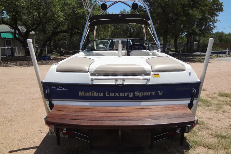 Slide: The Image of 2000 Malibu Sunsetter VLX boat, rear view, parked outdoors with trees in background. - 3