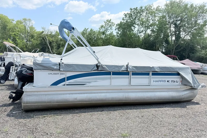 Slide: The Image of 2001 Harris Cruiser 220 pontoon boat with cover, parked on gravel, surrounded by trees. - 2