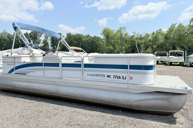 The Image of 2001 Harris Cruiser 220 pontoon boat with blue canopy, parked on gravel lot. - 0