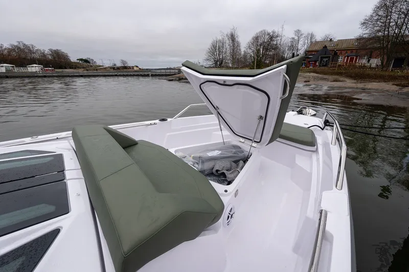 Slide: The Image of 2027 Axopar 38 Cross Cabin boat with open storage compartment, docked by a scenic shoreline. - 24