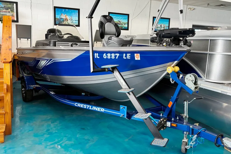 Slide: The Image of 2023 Crestliner 1650 Fish Hawk boat in showroom, blue and silver design, on trailer. - 0