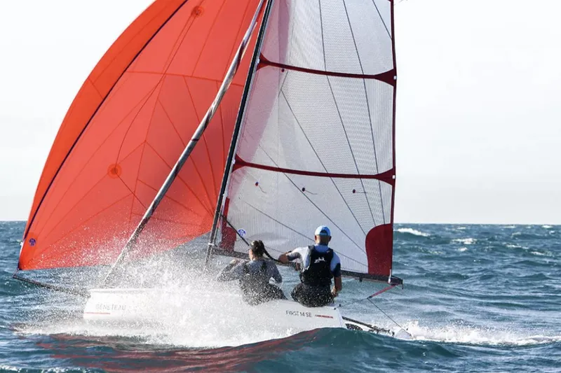 The Image of Manufacturer Provided Image: 2026 Beneteau First 14 SE sailboat with red sails navigating ocean waves. - 0