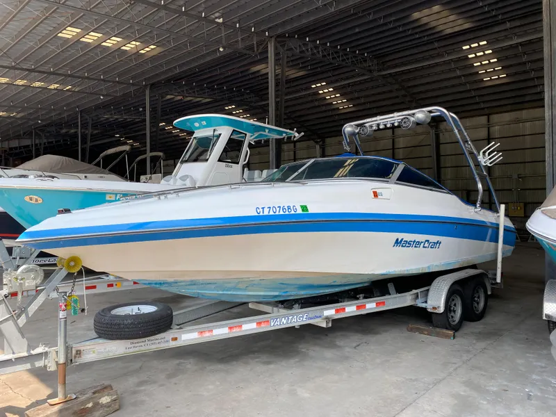 The Image of A 1990 MasterCraft Maristar 240 sits on a trailer in a warehouse. - 0