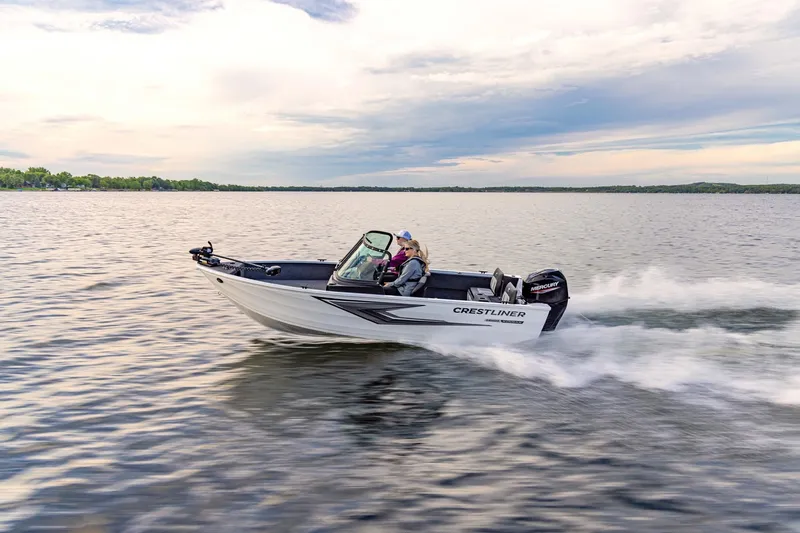 Slide: The Image of 2027 Crestliner 1650 Kodiak WT boat cruising on a serene lake under a cloudy sky. - 2