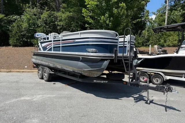 The Image of A 2019 Ranger Reata 200C pontoon boat on a trailer, surrounded by trees. - 1