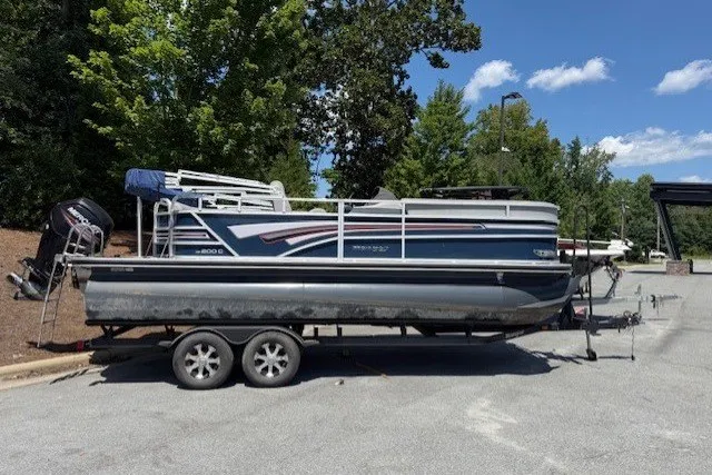 Slide: The Image of A 2019 Ranger Reata 200C pontoon boat on a trailer in a parking area, surrounded by trees. - 6