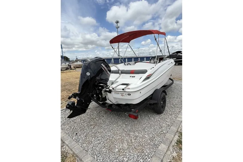 Slide: The Image of 2027 Tahoe T18 boat with Mercury engine, red canopy, parked on gravel. - 2