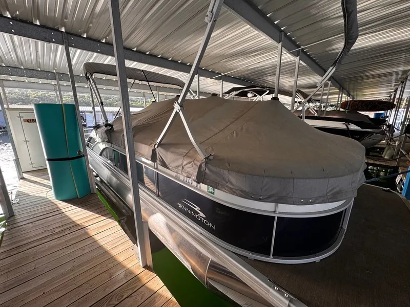 Slide: The Image of A 2023 Bennington 23SXSB pontoon boat is docked under a covered area, featuring a gray cover. - 11