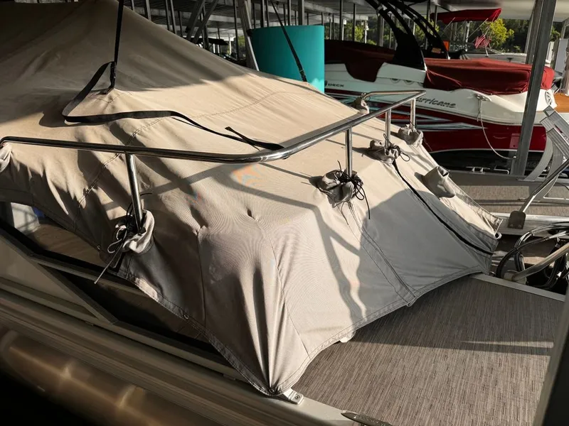 Slide: The Image of A 2023 Bennington 23SXSB with a cover in a marina. Other boats are visible in the background. - 13