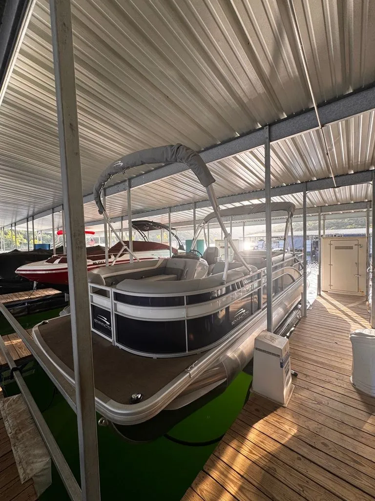 Slide: The Image of A 2023 Bennington 23SXSB pontoon boat is docked under a covered area. It features a sleek design. - 2